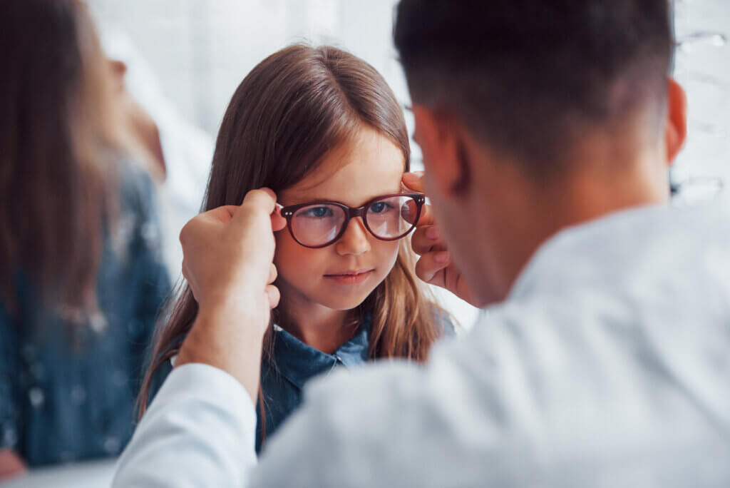 A young girl having glasses placed on her by an eye doctor